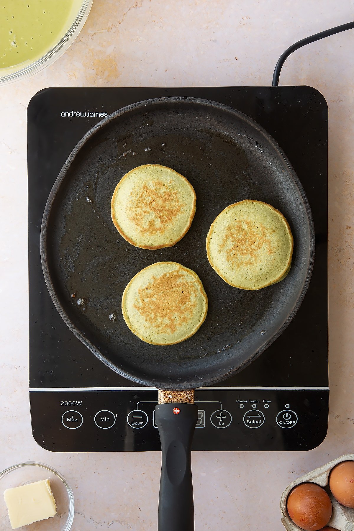 3 cooked matcha pancakes in a frying pan on an induction hob