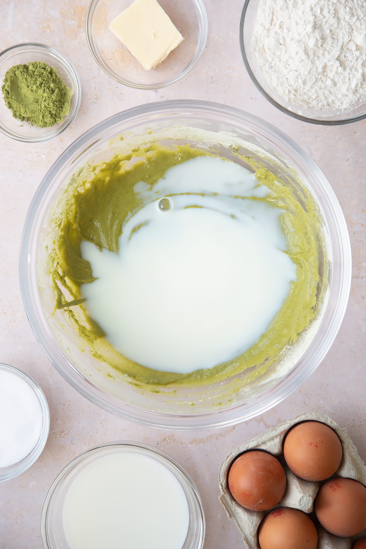 mixed matca pancake mix in a large clear bowl topped with milk surrounded by ingredients.