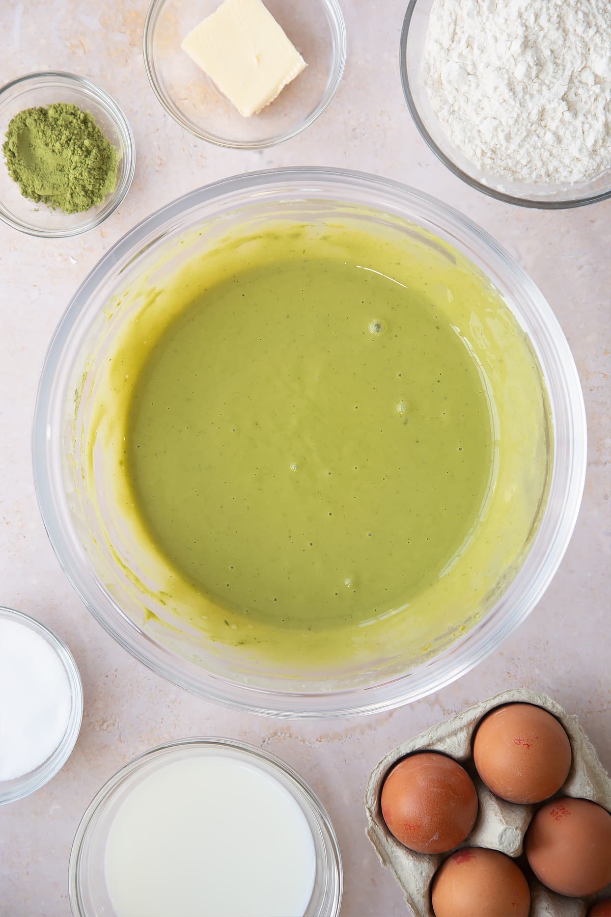 smooth matcha pancake mix in a large clear bowl surrounded ingredients.