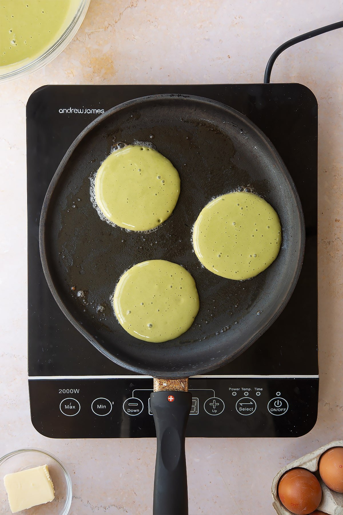 3 raw matcha pancakes in a frying pan on an induction hob.