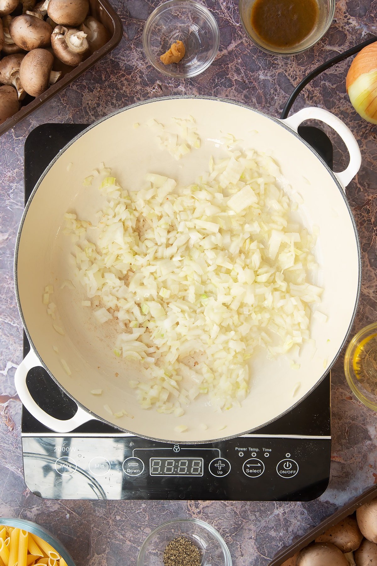 diced onions in a large white frying pan on an induction hob.