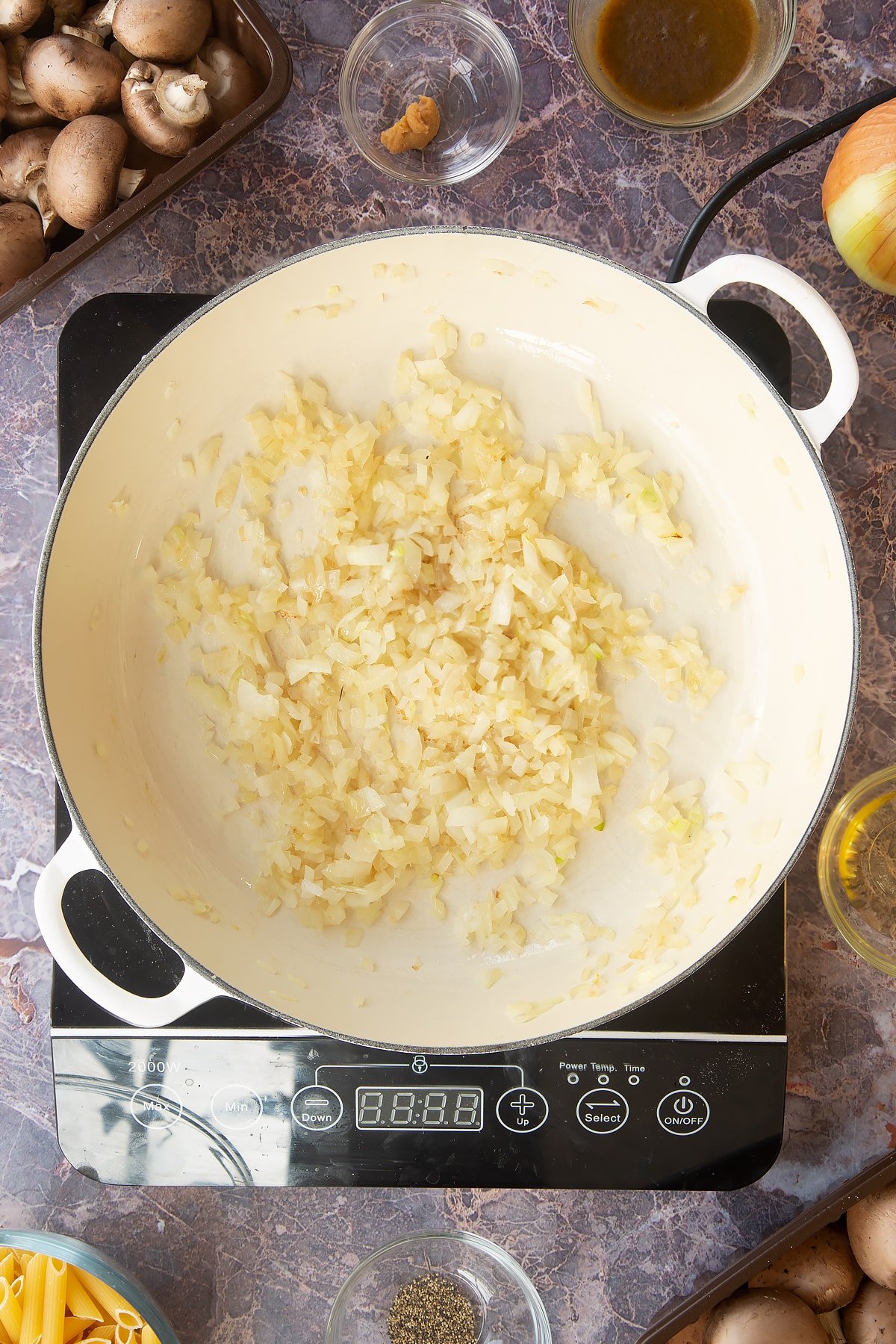 cooked diced onions in a large white frying pan on an induction hob.