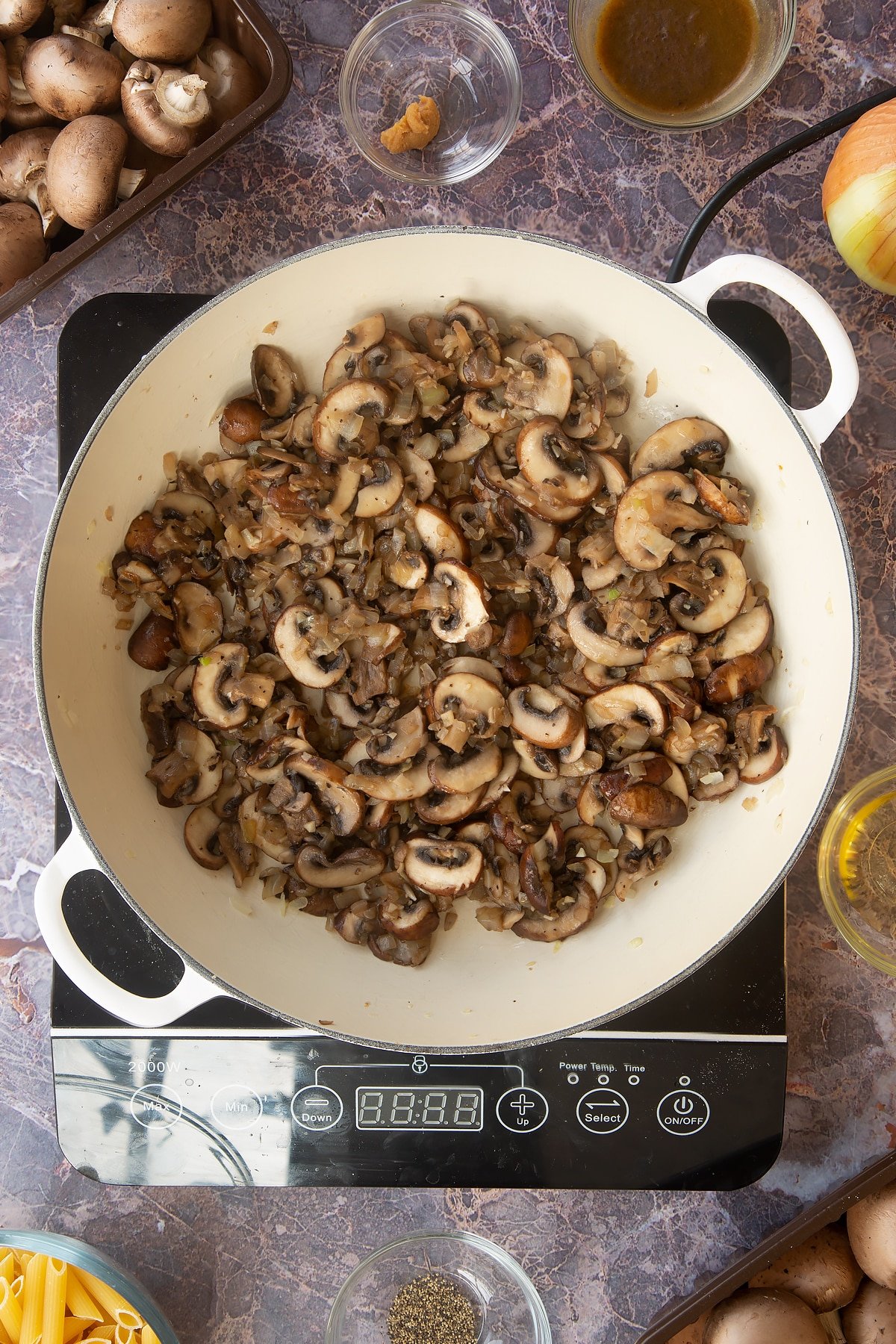 cooked mushroom, garlic and onion mix in a large white frying pan on an induction hob.