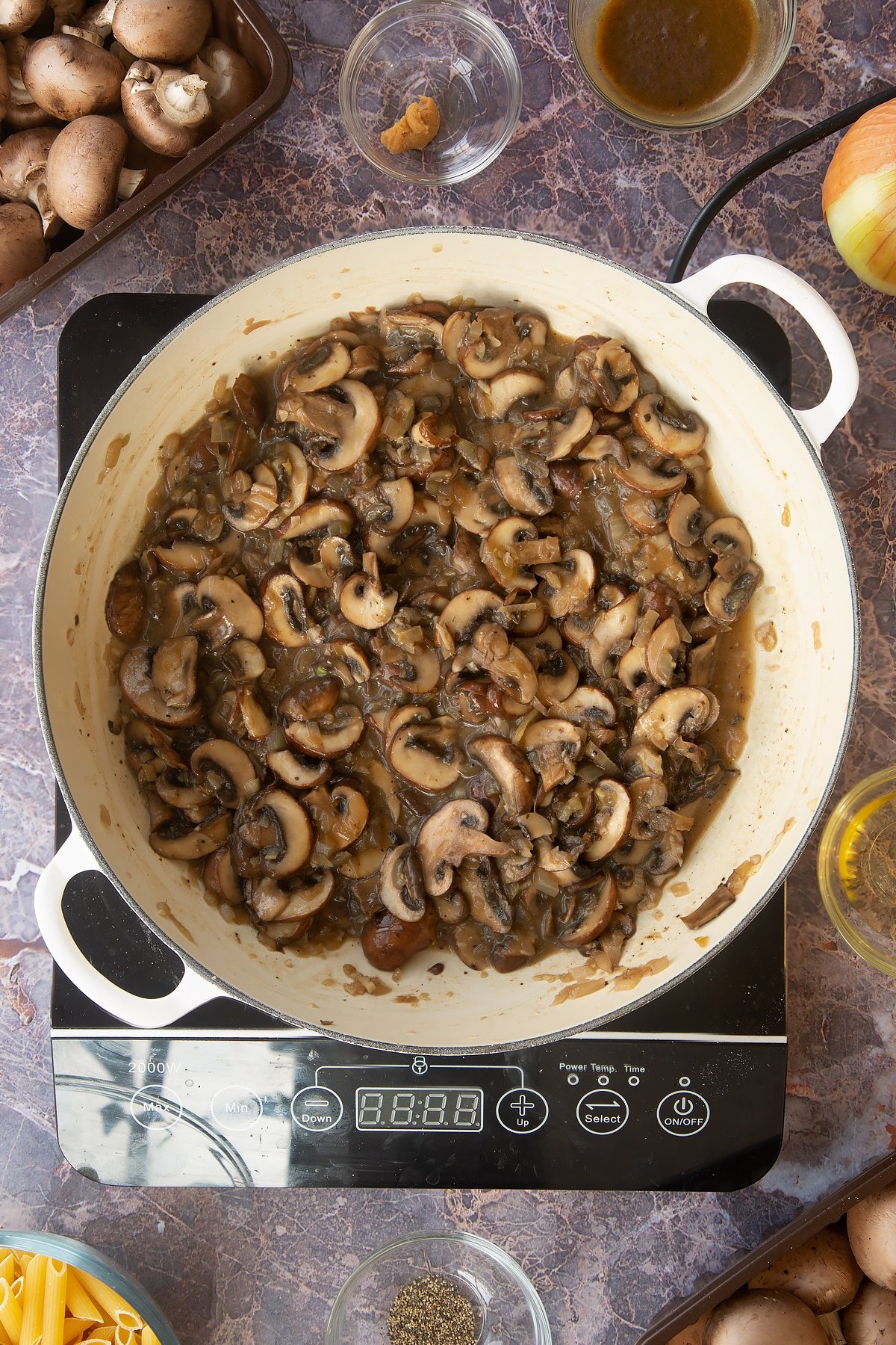 cooked mushroom, garlic and onion mix in a large white frying pan on an induction hob.