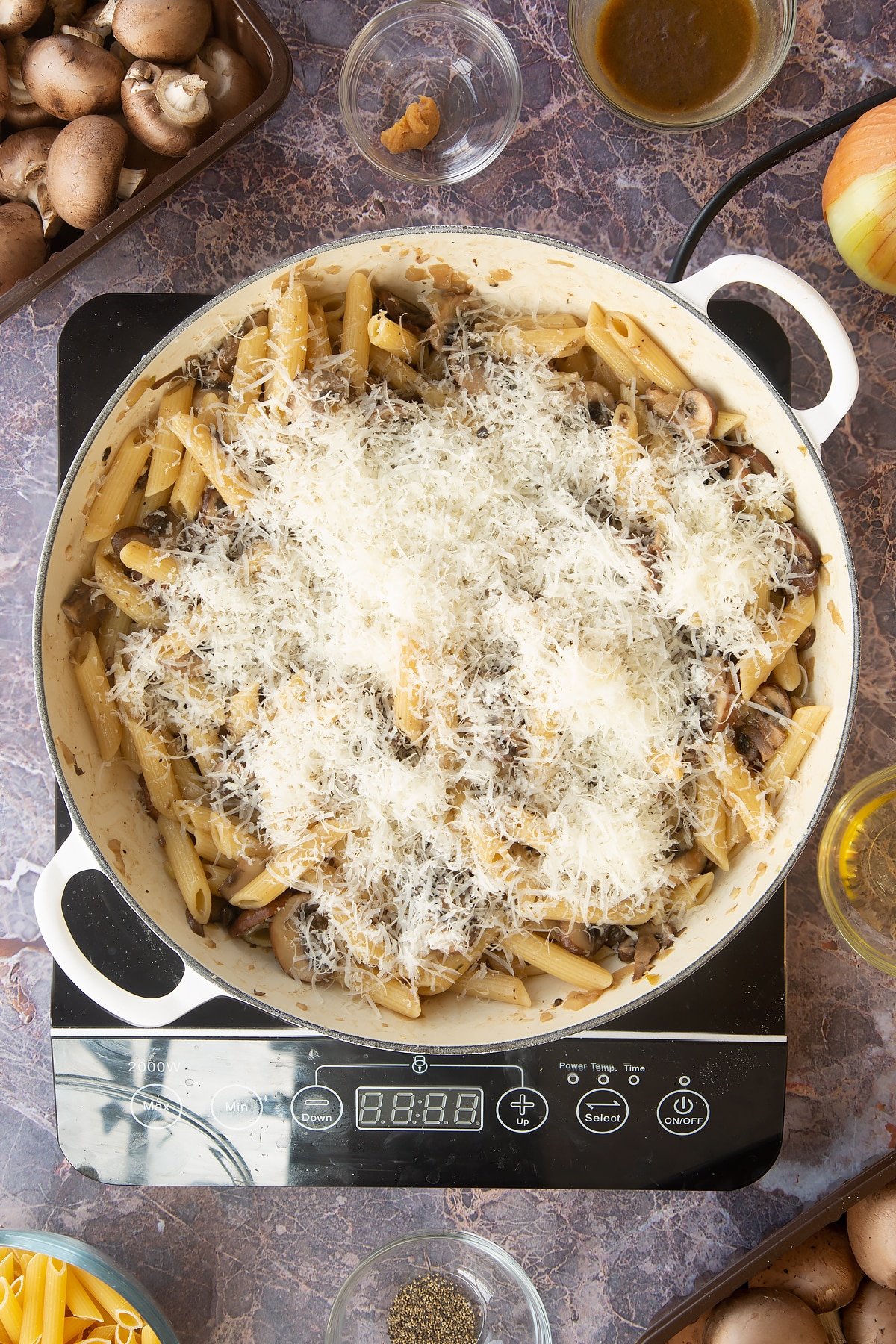 miso mushroom pasta cooked and mixed together in a large frying pan topped with grated cheese on an induction hob.