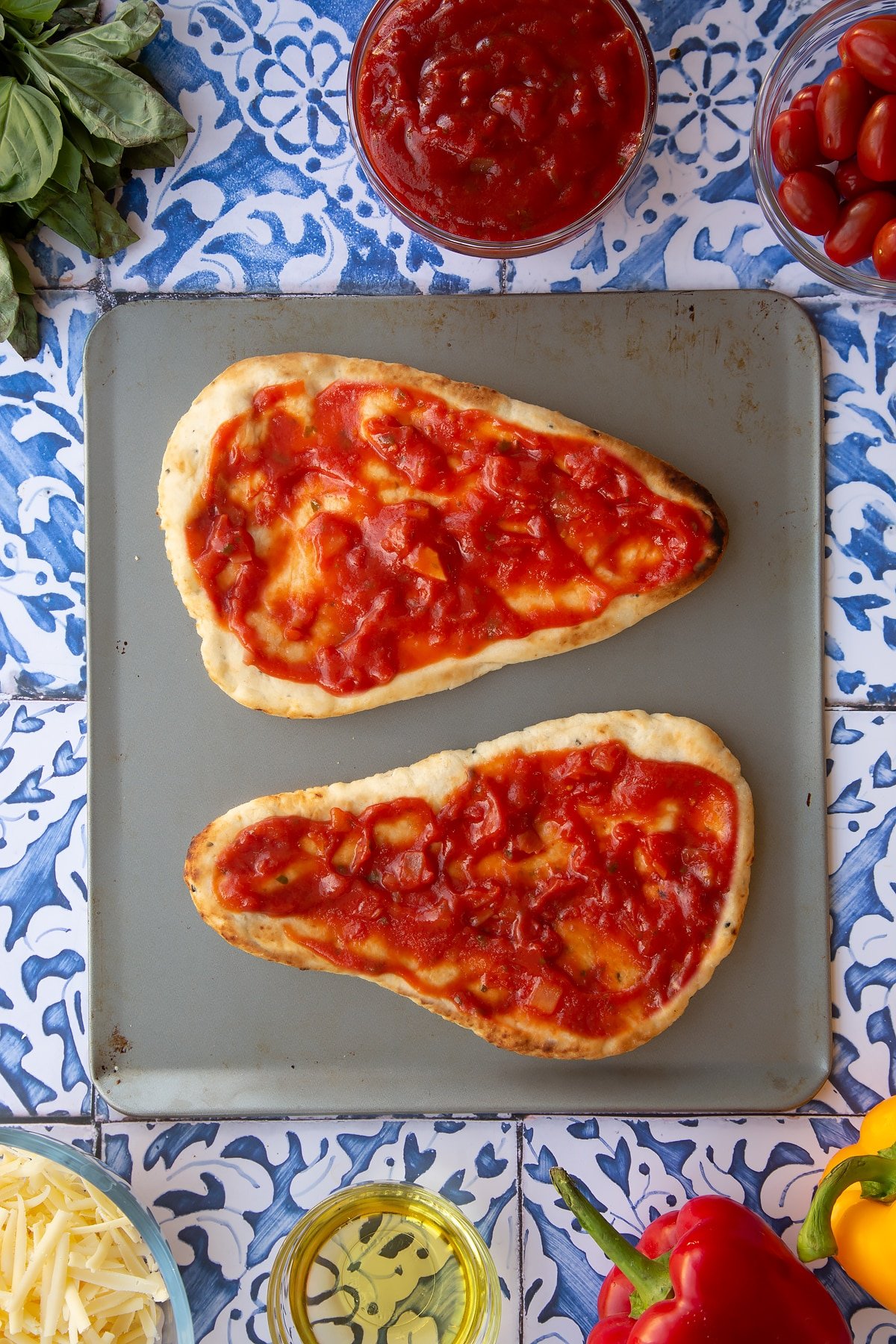 Two naan breads on top of a baking tray covered in tomato sauce.