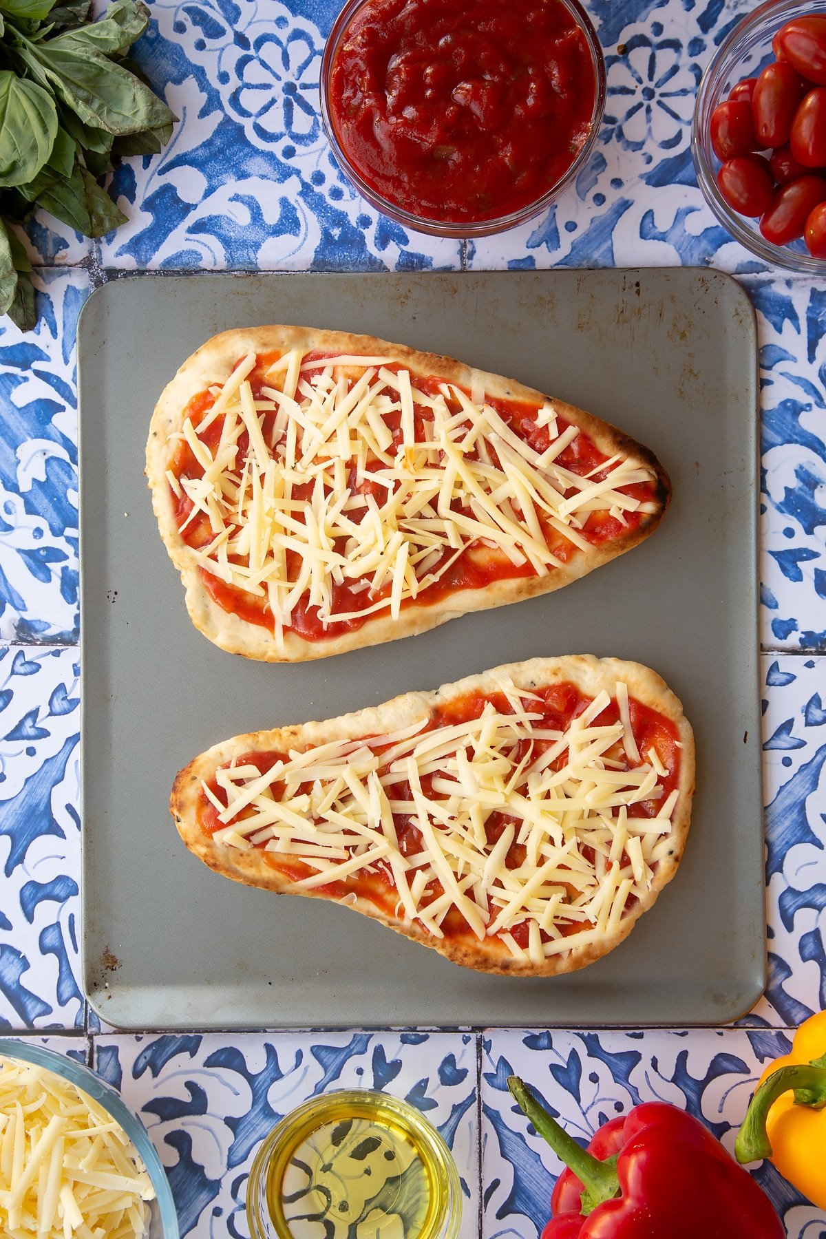 Two naan breads covered in tomato sauce and grated cheese sit on top of a square baking dish.