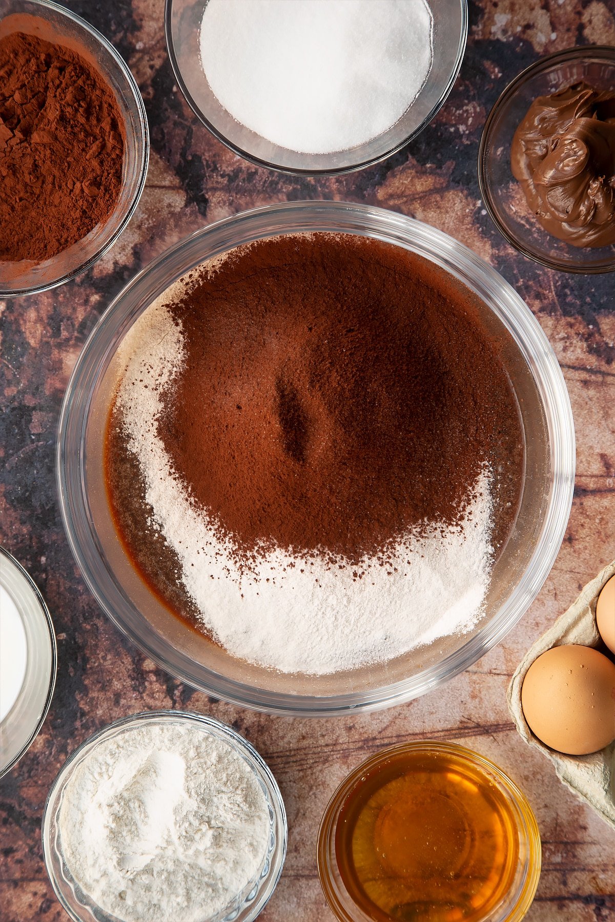 mixed wet ingredients topped with cocoa powder and flour in a clear bow;