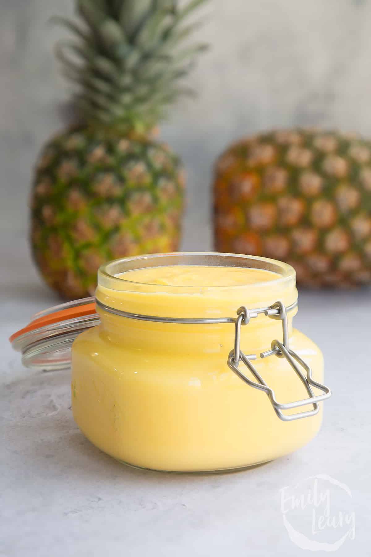 pineapple curd mixture in a glass jar with pineapples in the background.