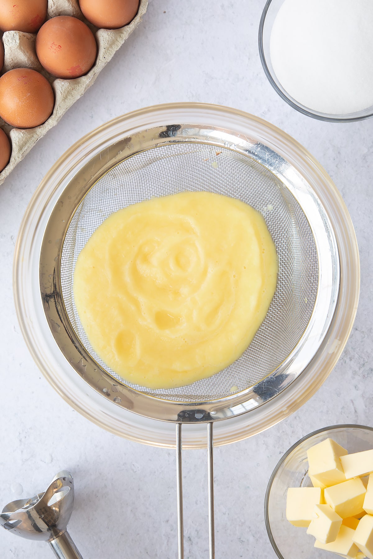 puree'd pineapple in a sieve over a large clear bowl surrounded by ingredients.