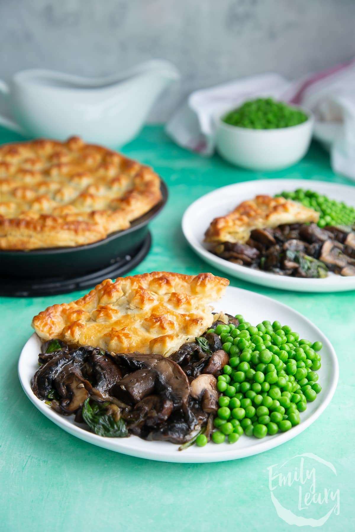 a slice of Spinach and mushroom pie on a white plate with green peas on the side.