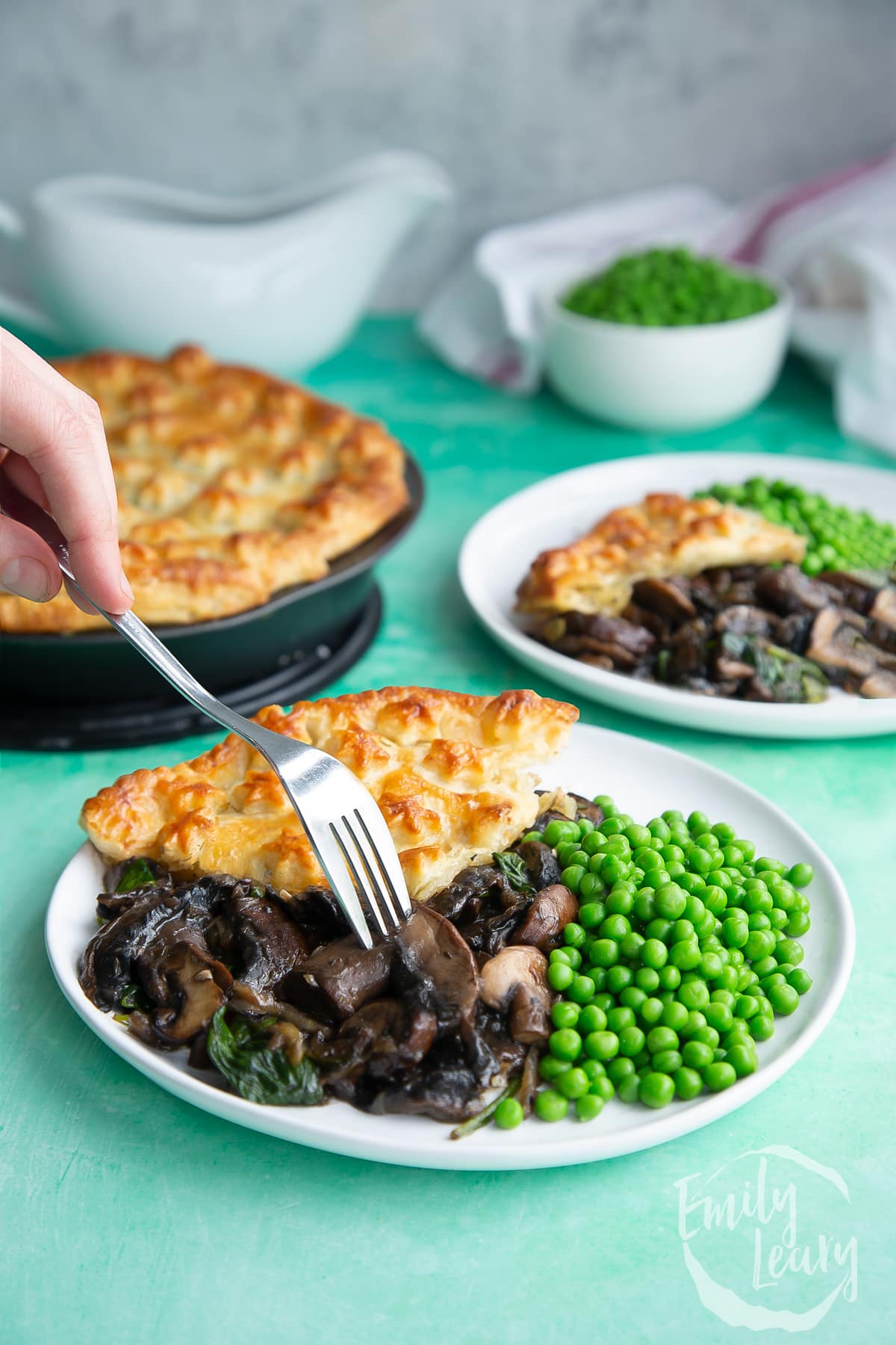 a slice of Spinach and mushroom pie on a white plate with green peas on the side and a fork at the front.