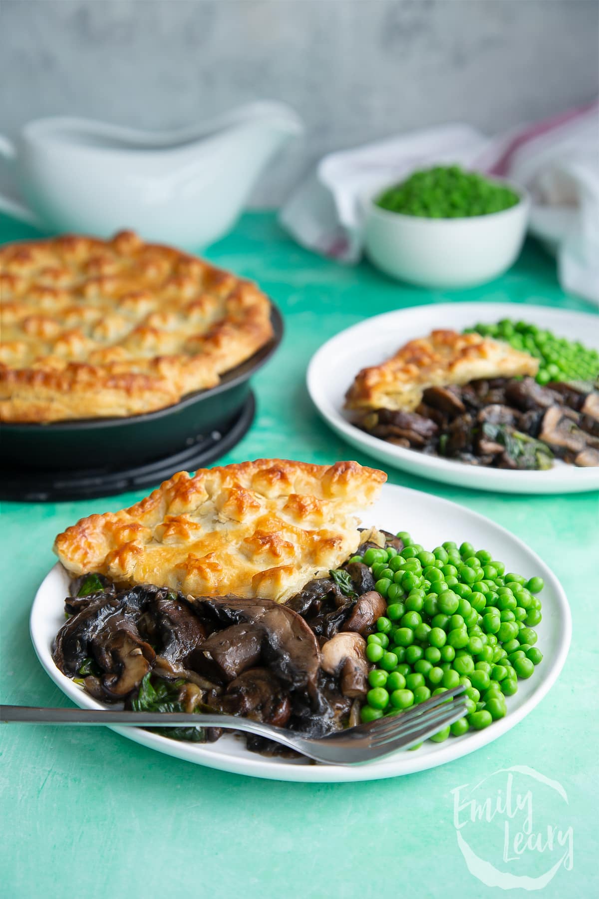 a slice of Spinach and mushroom pie on a white plate with green peas on the side and a fork at the front.