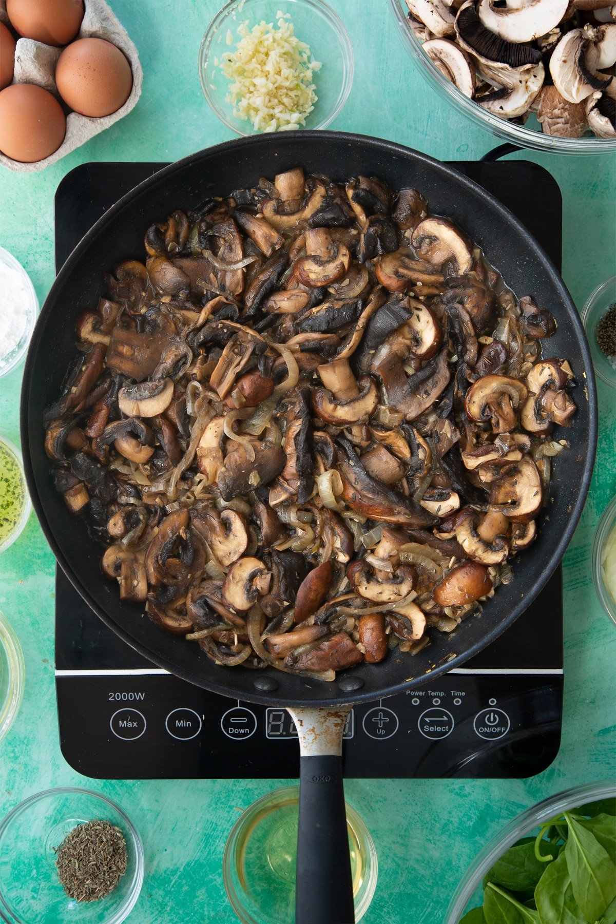 a large frying pan with cooked onions, herbs and garlic in a white wine sauce topped with sliced mushrooms.