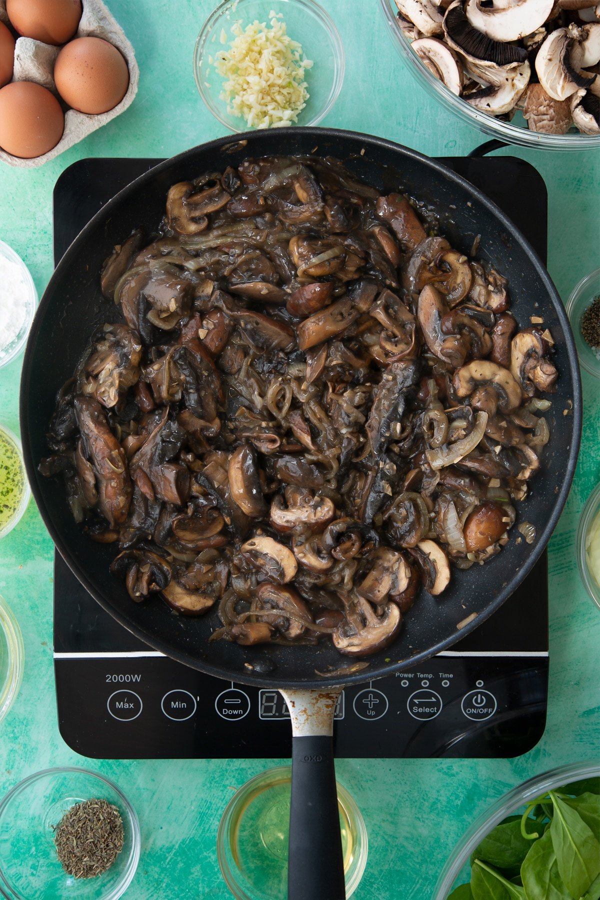 a large frying pan with cooked onions, herbs and garlic in a white wine sauce topped with sliced mushrooms.