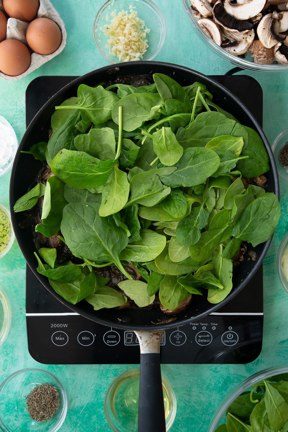 a large frying pan with cooked onions, herbs and mushrooms in a white wine sauce topped with spinach.