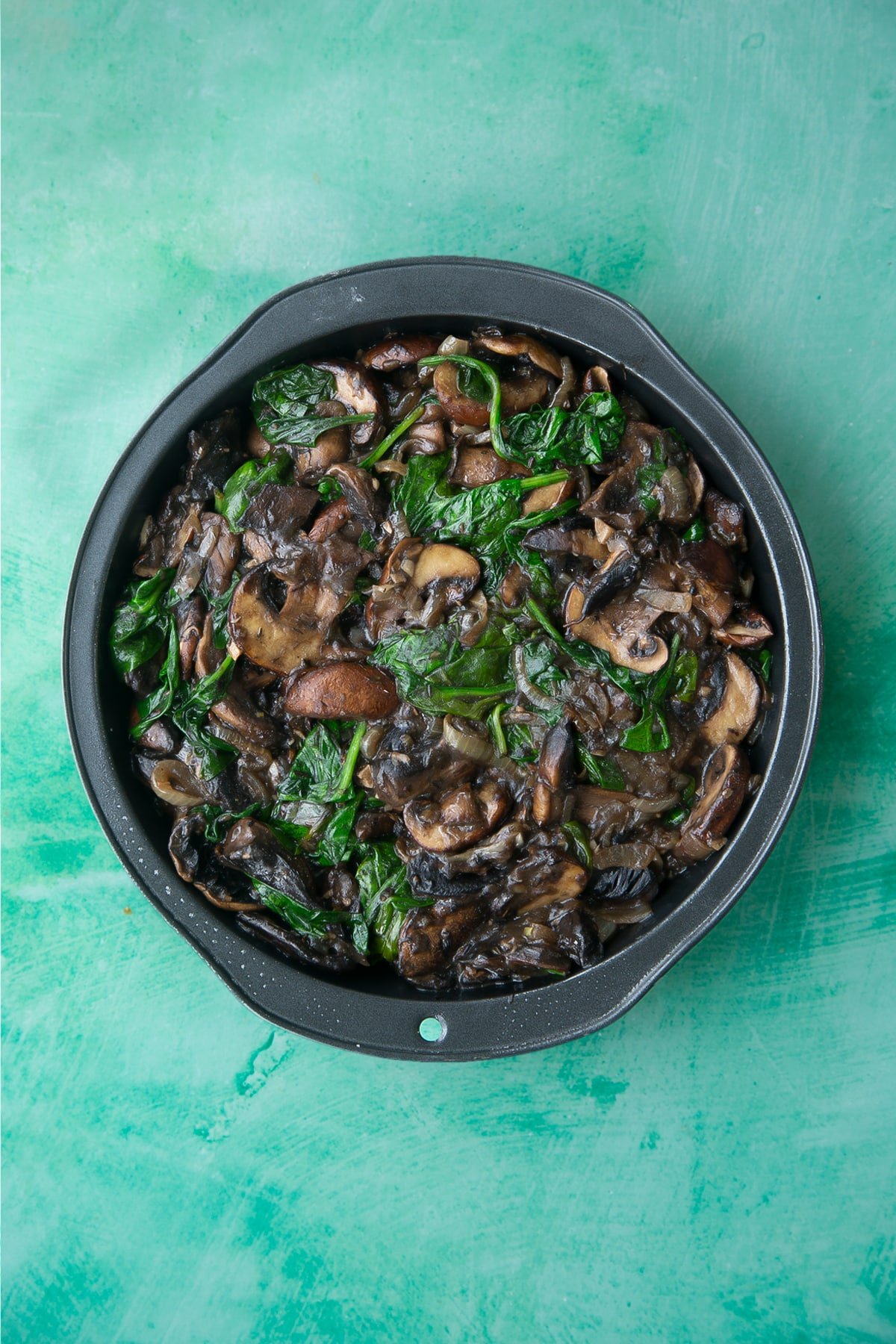 cooked onions, mushrooms and spinach in a white wine sauce in a pie dish.