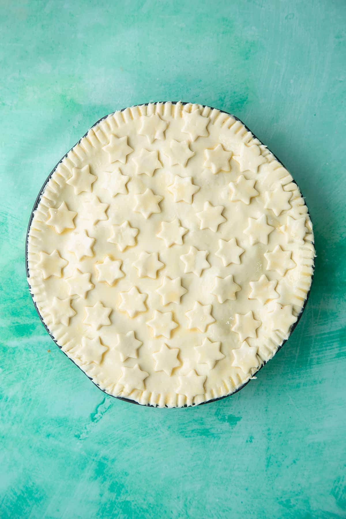 a pie dish topped with pastry and pastry stars brushed with egg.