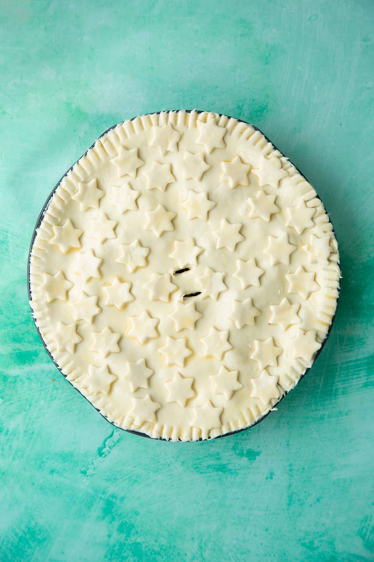 a pie dish topped with pastry and pastry stars brushed with egg and two holes in the middle.