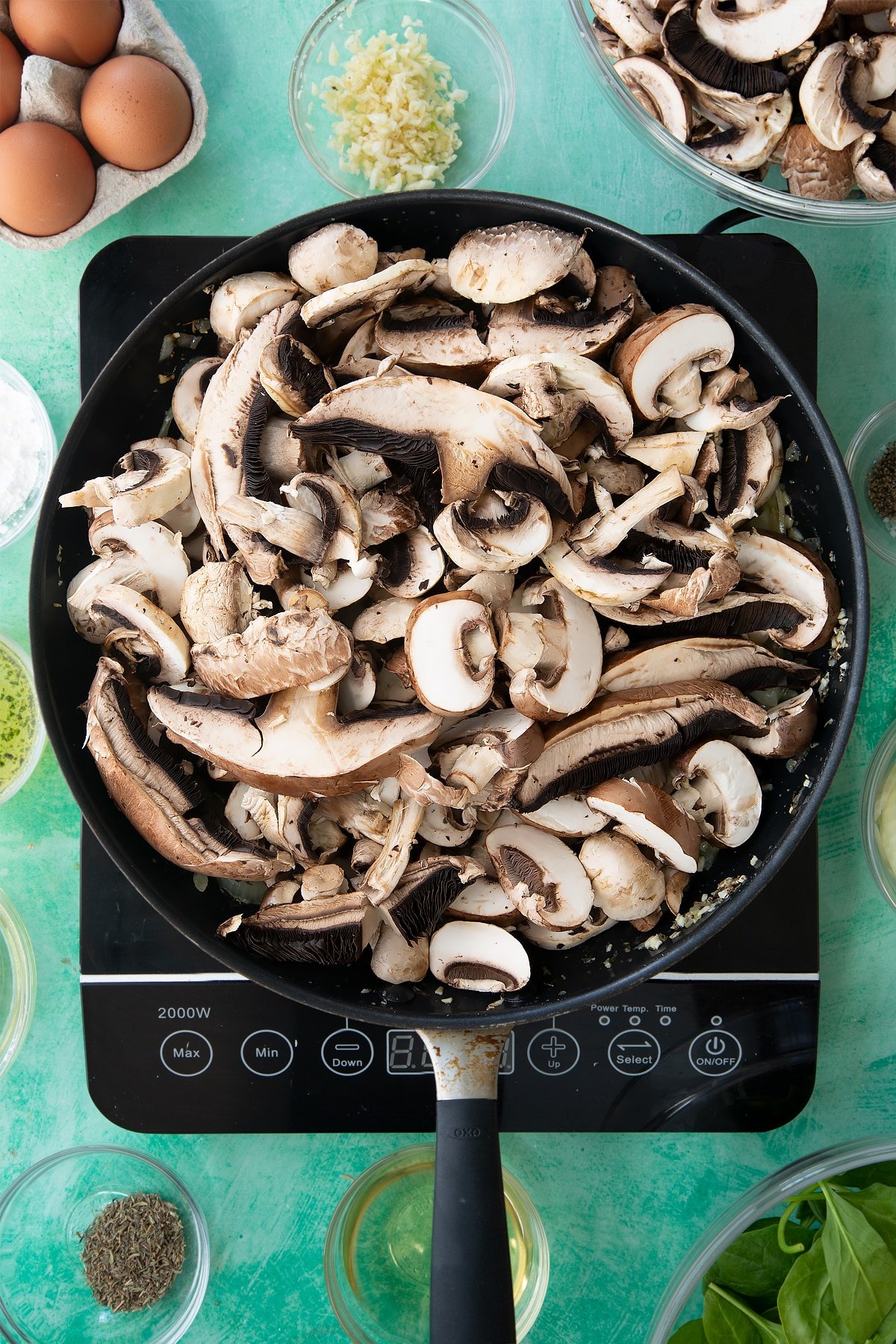 a large frying pan with cooked onions, herbs and garlic in a butter sauce topped with sliced mushrooms.