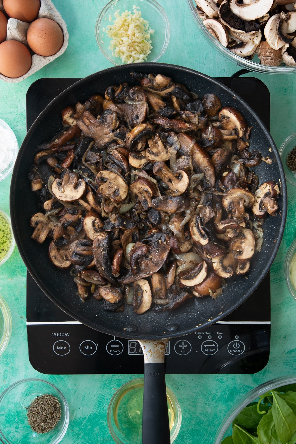 a large frying pan with cooked onions, herbs and garlic in a butter sauce topped with sliced mushrooms.