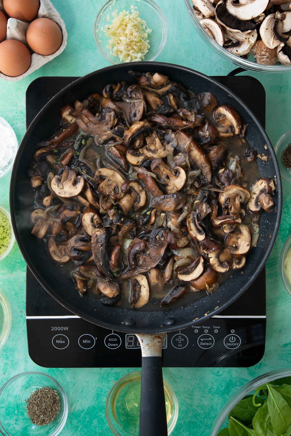 a large frying pan with cooked onions, herbs and garlic in a white wine sauce topped with sliced mushrooms.