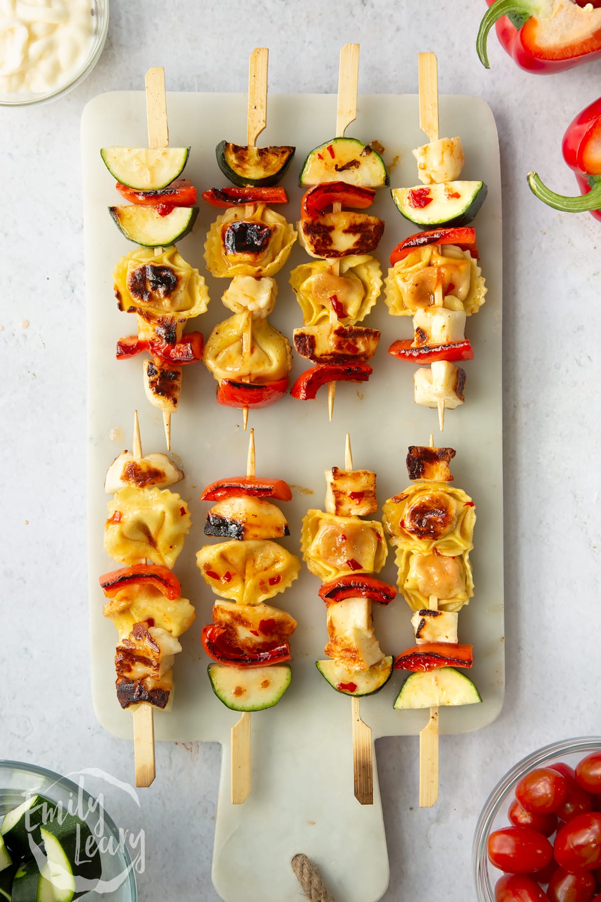 Sweet chilli halloumi kebabs laid on a marble surface with vegetables around the sides.