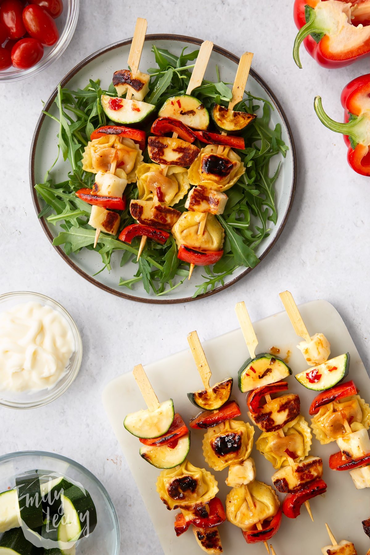 Sweet chilli halloumi kebabs on a bed of rocket on a white plate next to more Sweet chilli halloumi kebabs on a marble board.