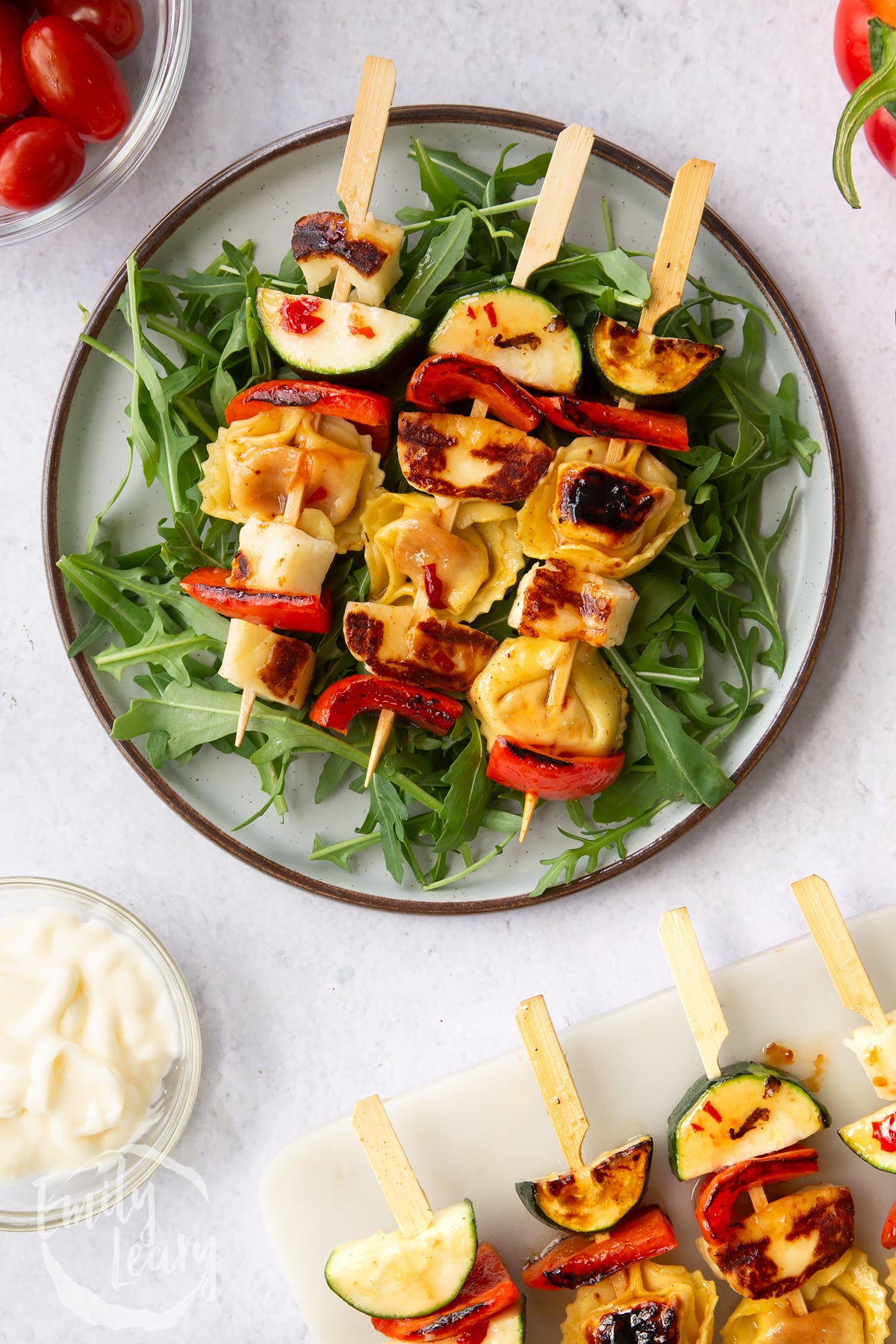 3 halloumi and red pepper skewers on a bed of salad on a white plate.