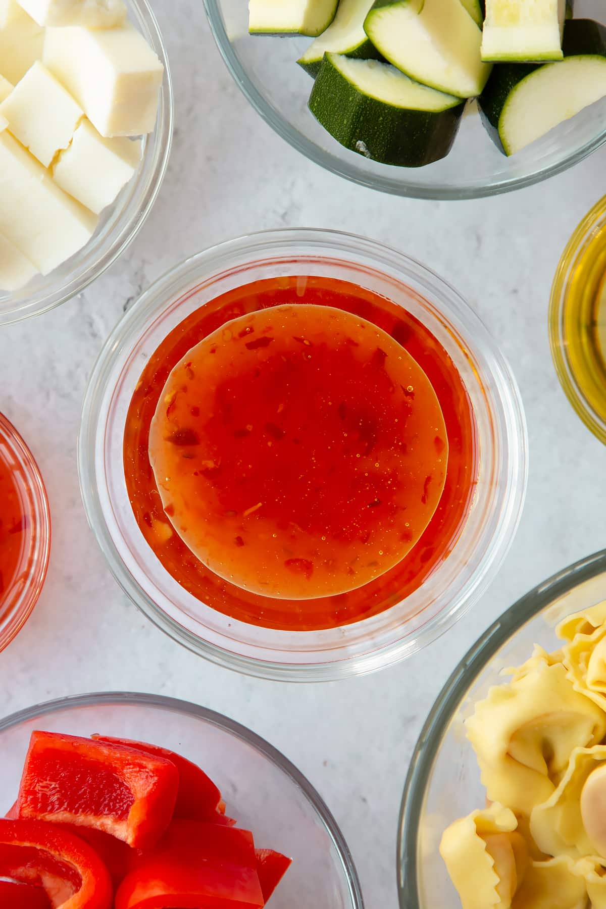 sweet chilli sauce mixed with olive oil in a clear bowl surrounded by ingredients.