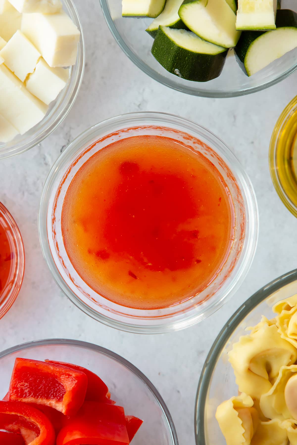 sweet chilli sauce mixed with olive oil in a clear bowl surrounded by ingredients.