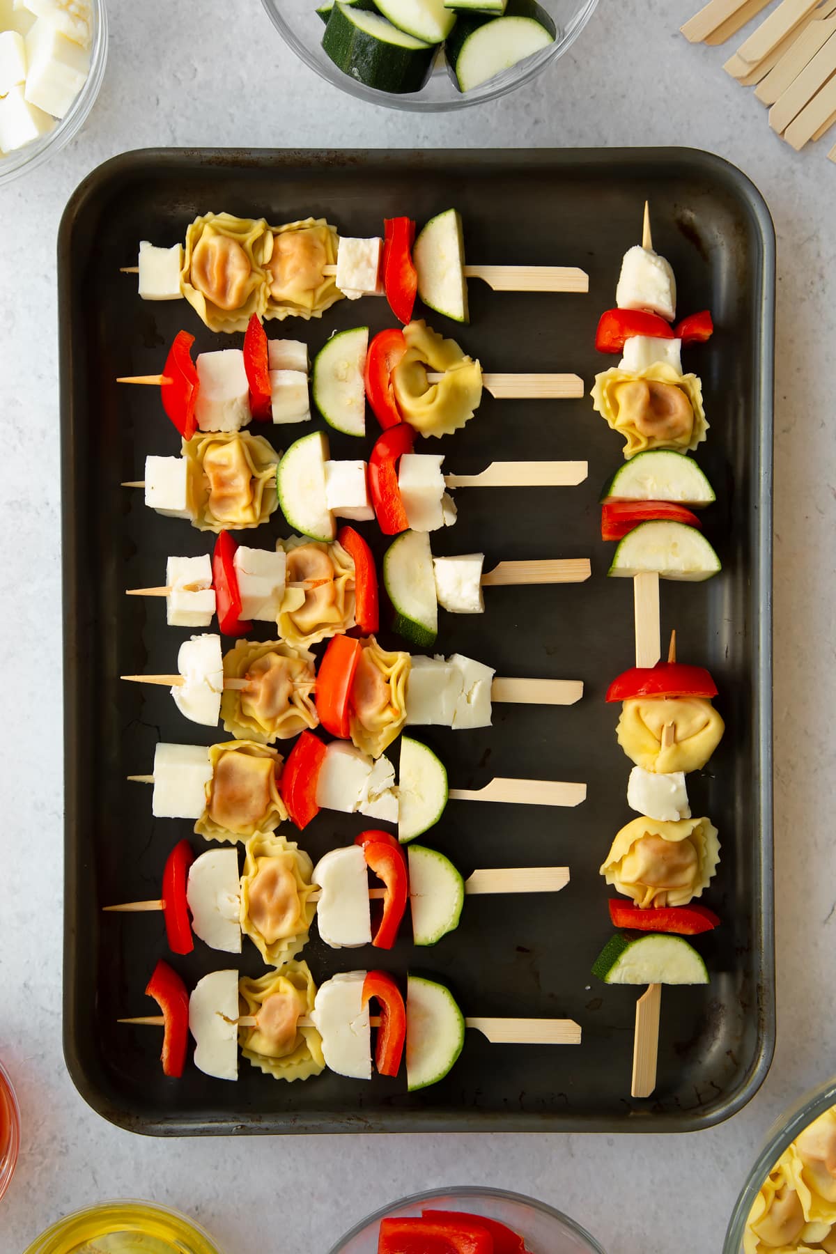 raw courgette, tortellini, halloumi and red pepper on wooden skewers placed on a baking tray.
