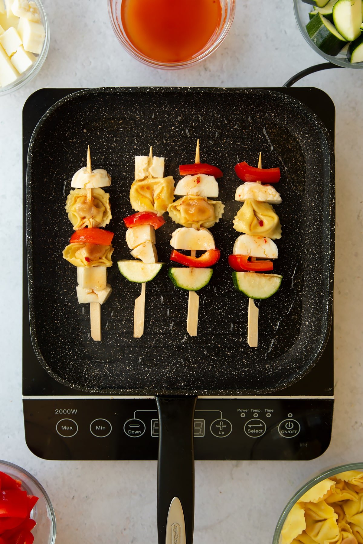 a frying pan on an induction hob with 4 halloumi skewers inside cooking in oil.