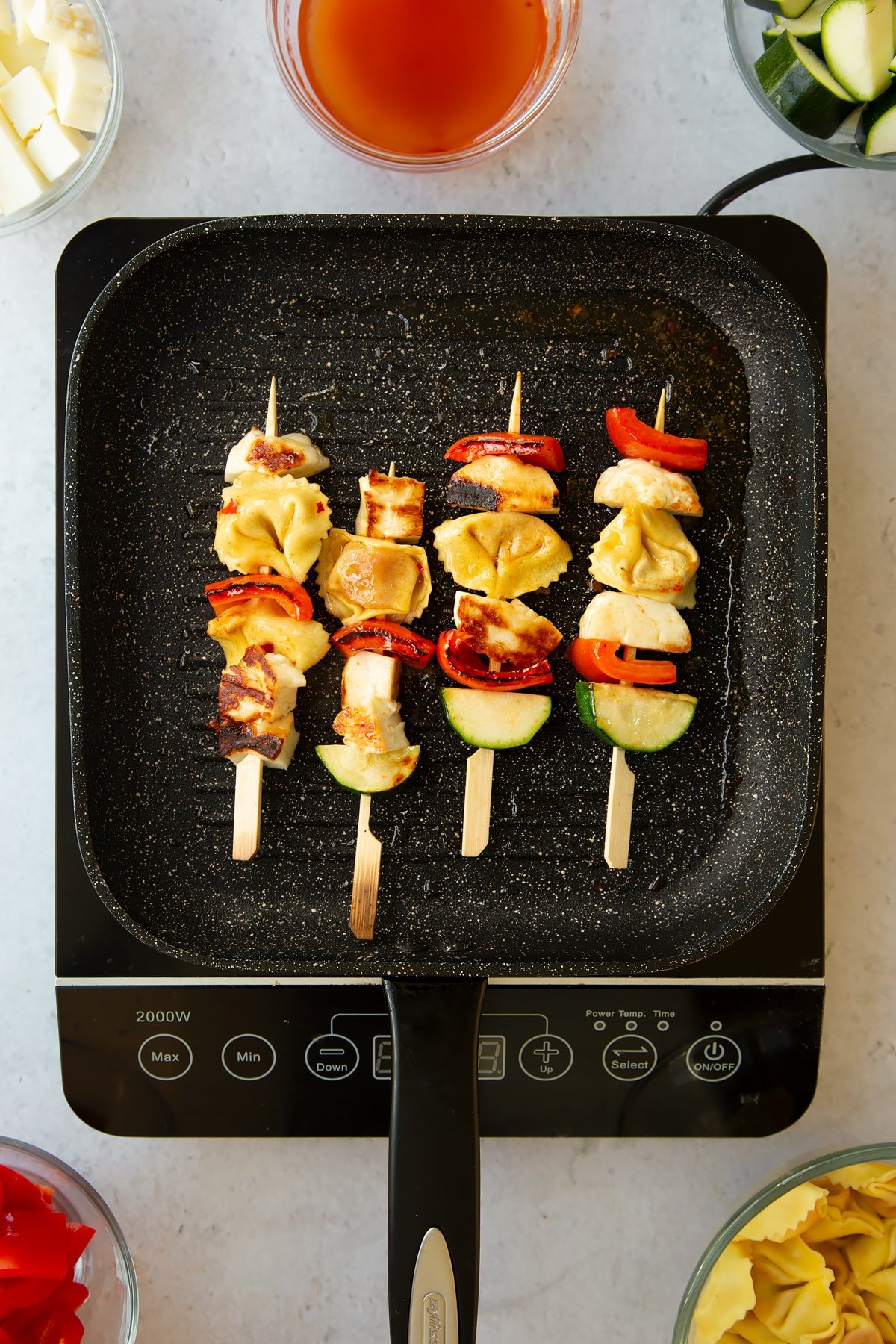 a frying pan on an induction hob with 4 halloumi skewers inside cooking in oil.