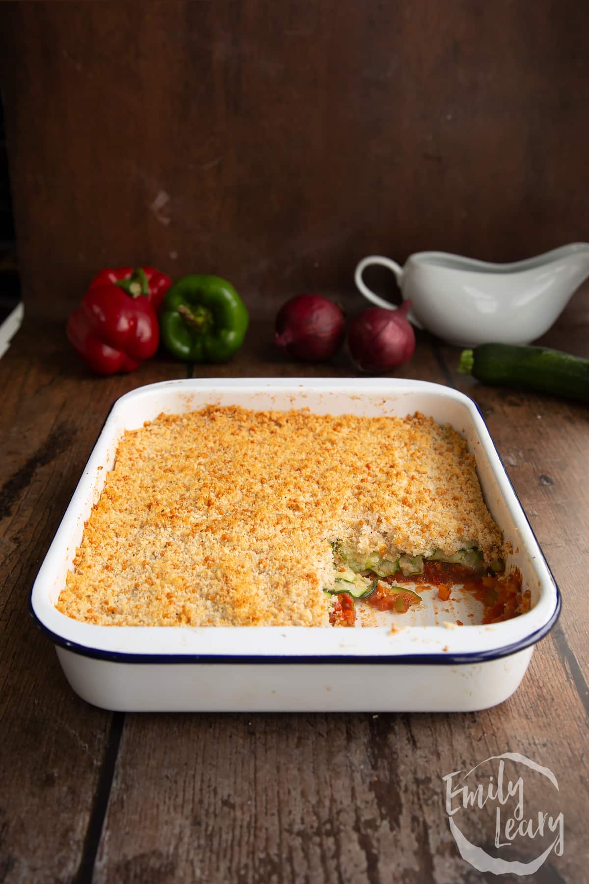 Tomato and courgette gratin in a white baking dish eith a piece cut out of the corner.