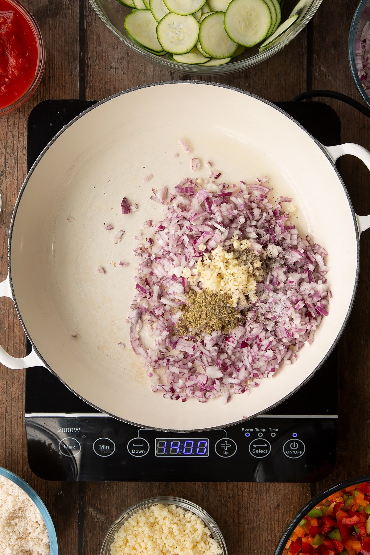 a large frying pan with a dash of oil, diced red onion, garlic and oregano on an induction hob.