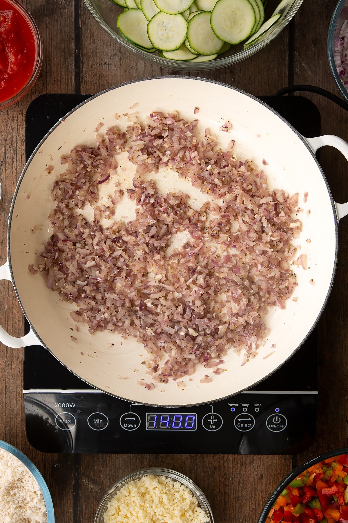 cooked dred onion and garlic mix in a large white frying pan on induction hob.