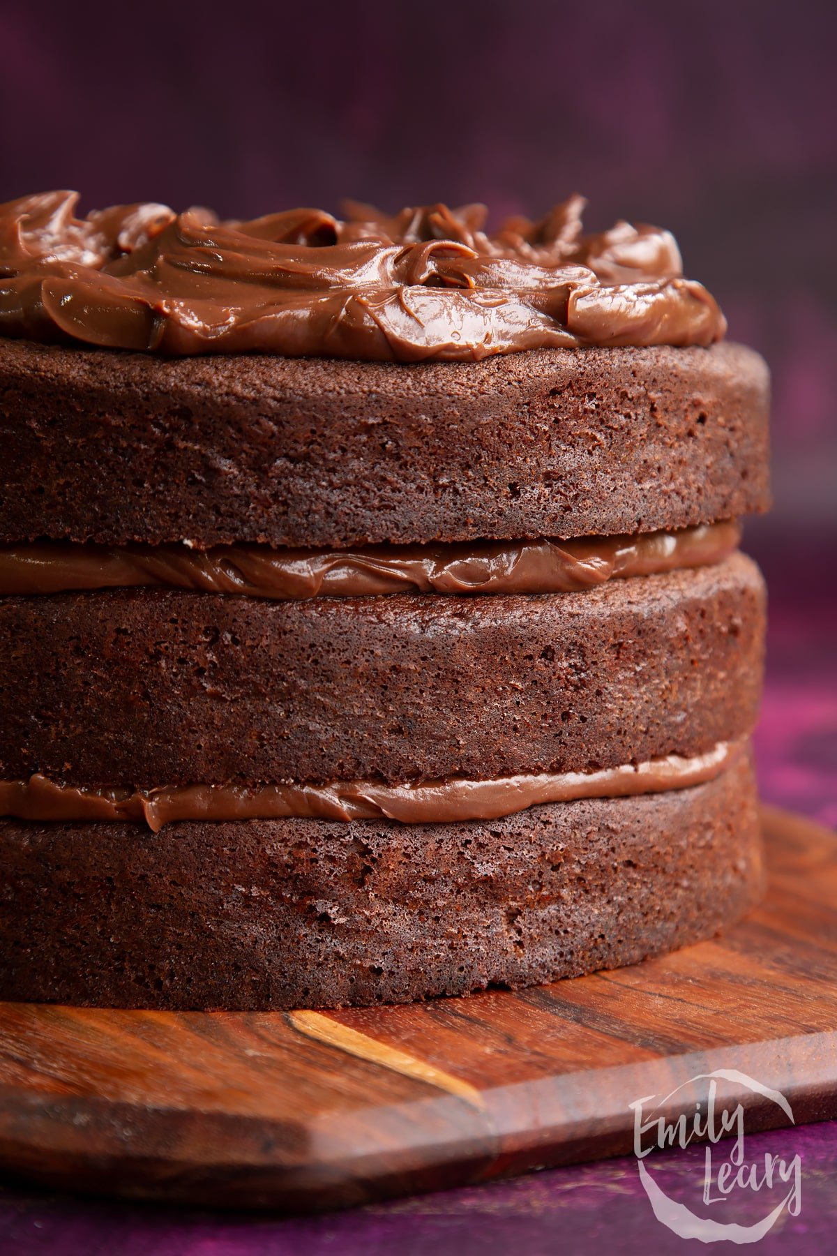 side view of Ultimate chocolate fudge cake on a wooden chopping board.