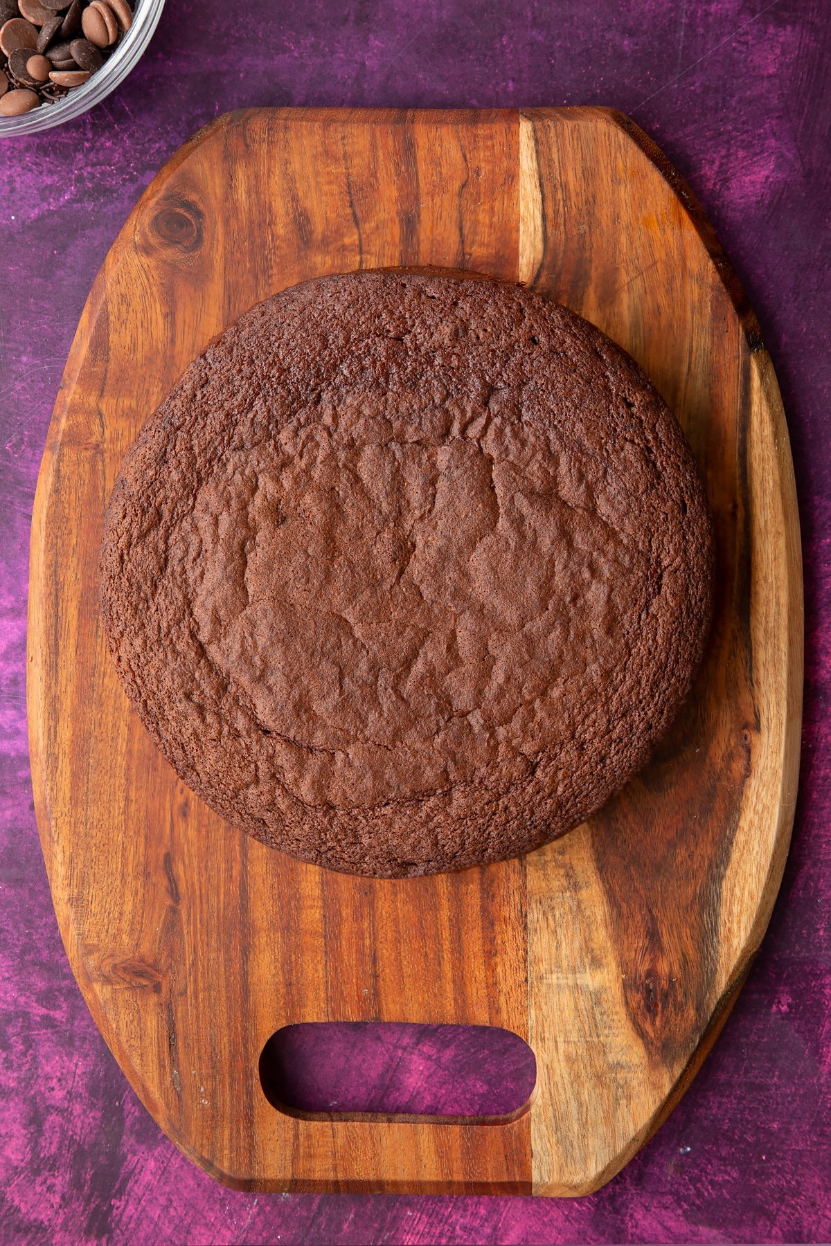 a large round chocolate sponge cake on a wooden chopping board.