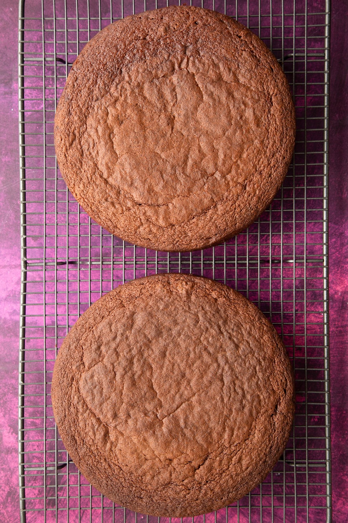 2 cooked round chocolate cakes on a wire cooling rack.