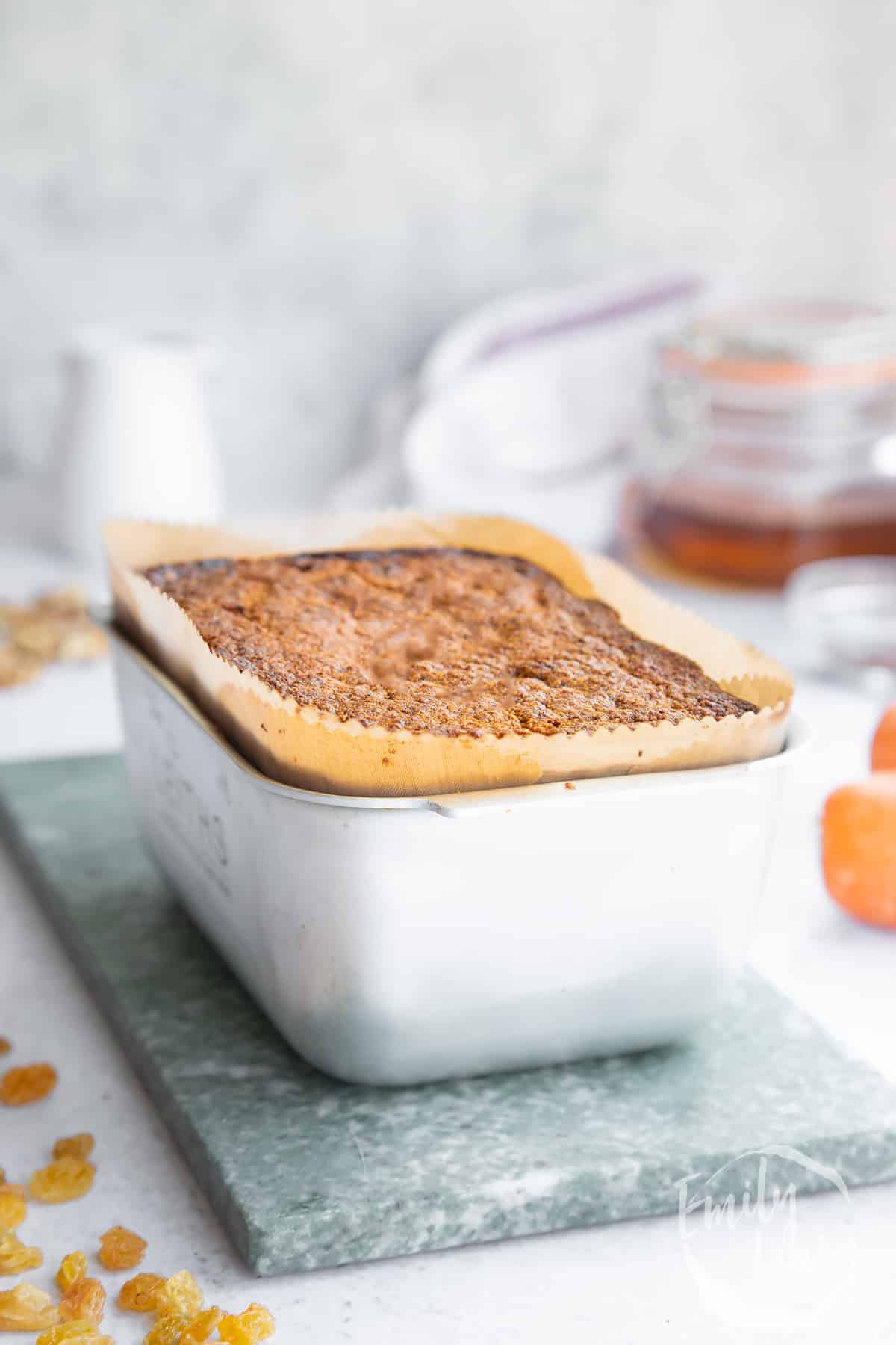 cooked vegan carrot cake in a lined loaf tin with ingredients in the background.