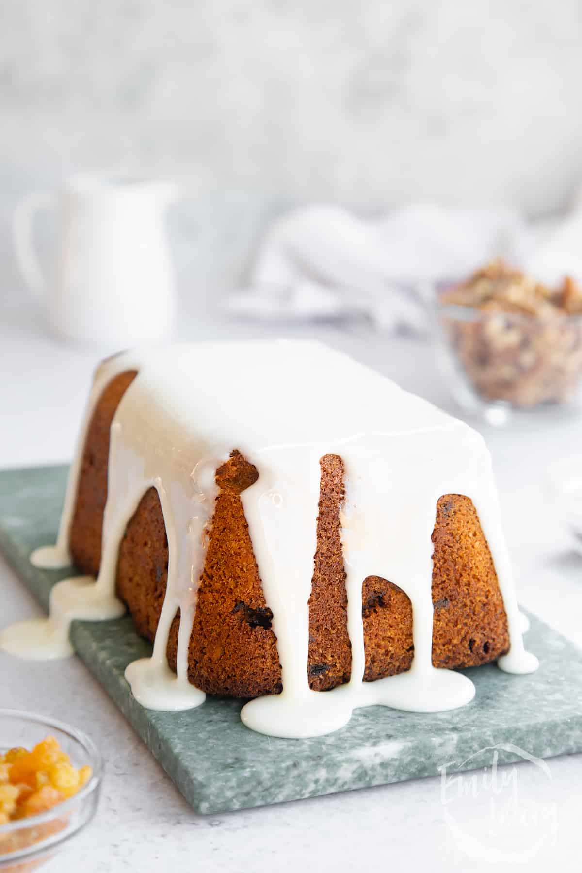 a Vegan carrot loaf cake drizzled with icing on a marble board.