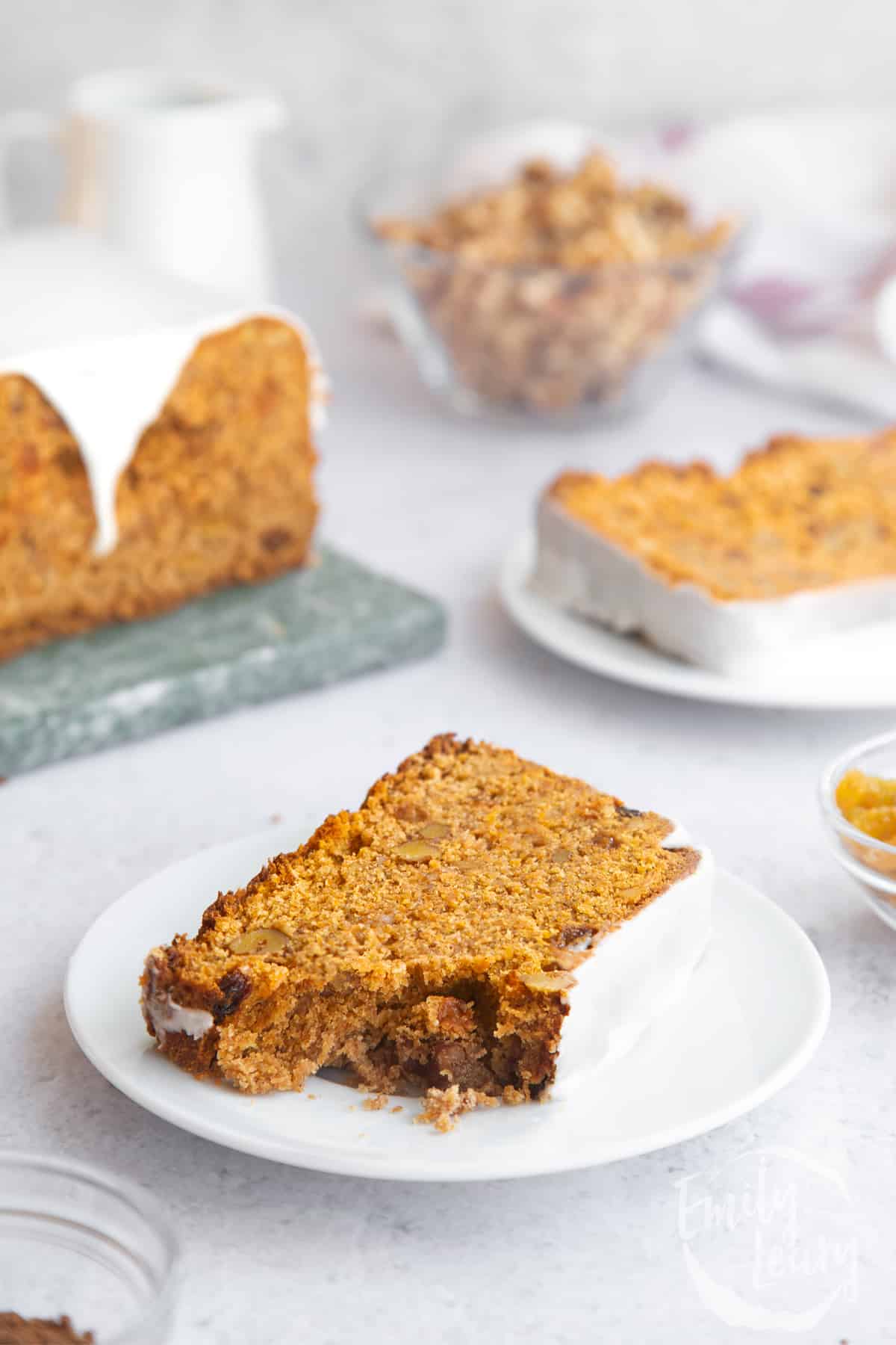 a slice of vegan carrot cake loaf on a white plate topped with icing.