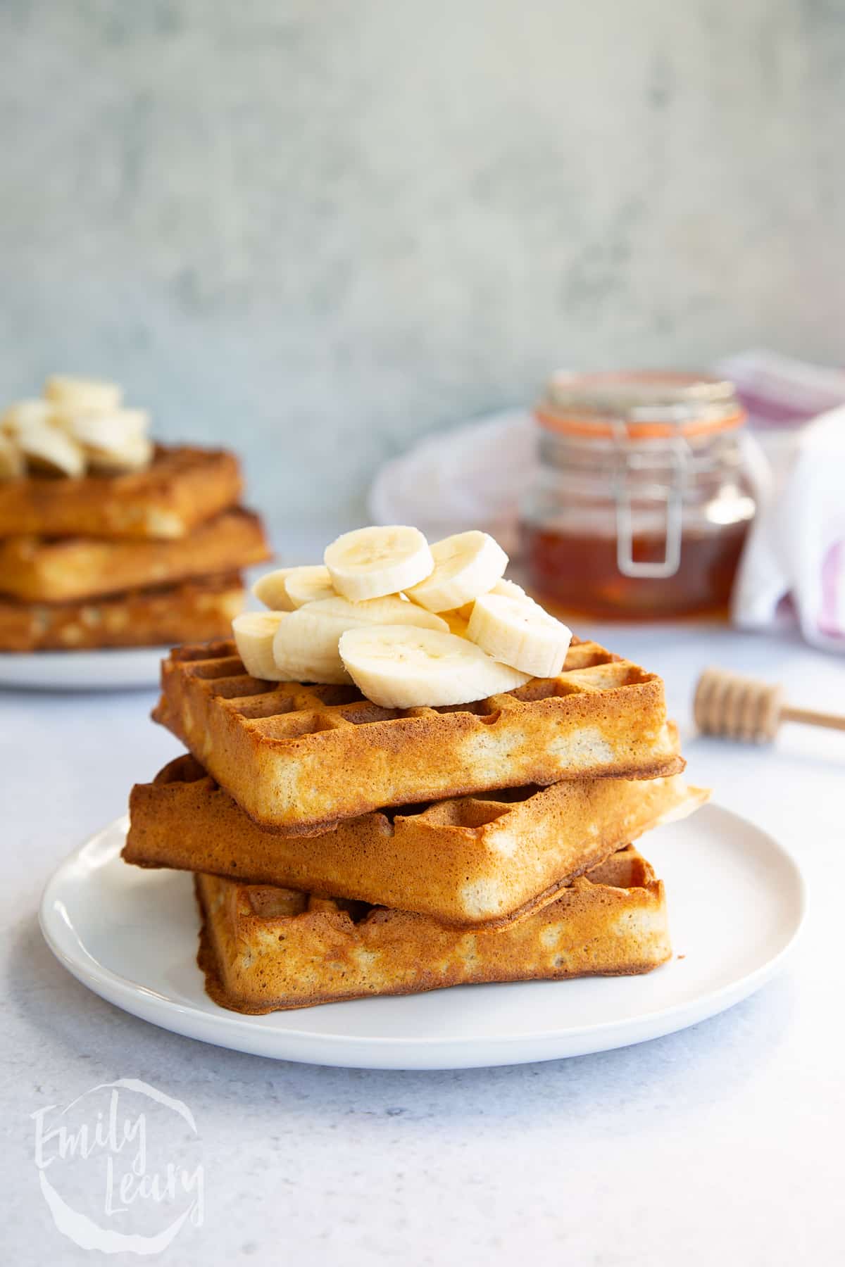 a stack of 3 wholemeal pancakes on a white plate topped with slices of banana.