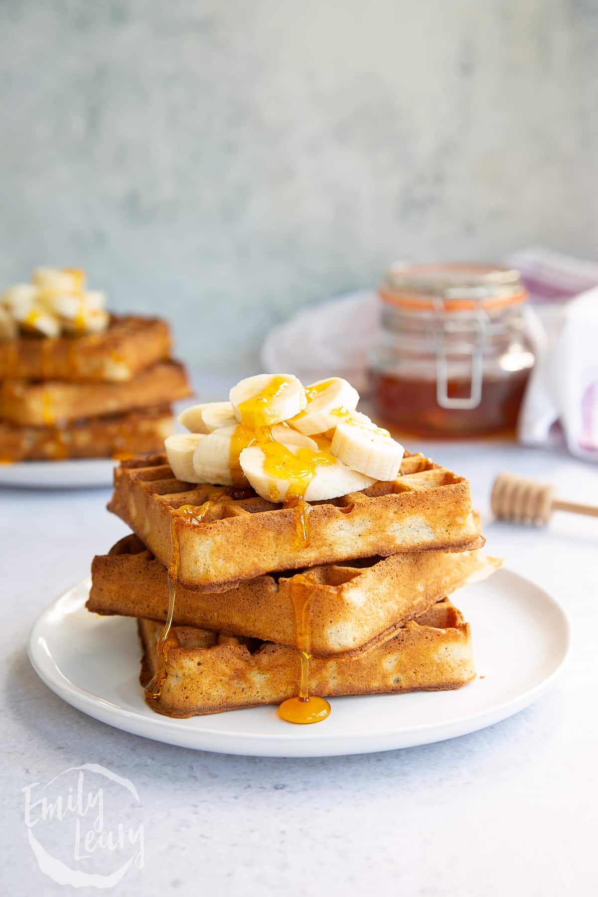 a stack of wholemeal waffles on a white plate topped with honey and banana,