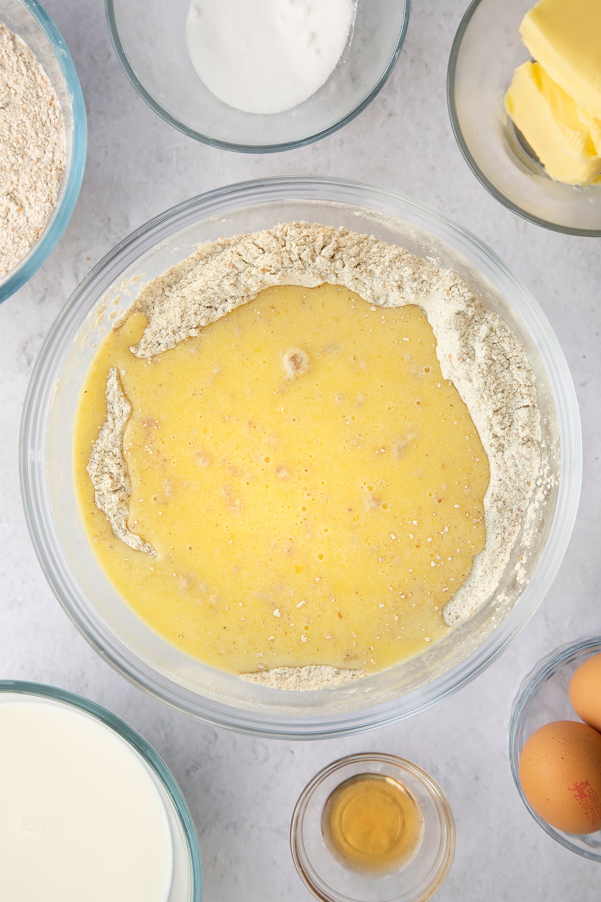 wholemeal flour mixtyure topped with egg and melted butter mixture in a large clear bowl.