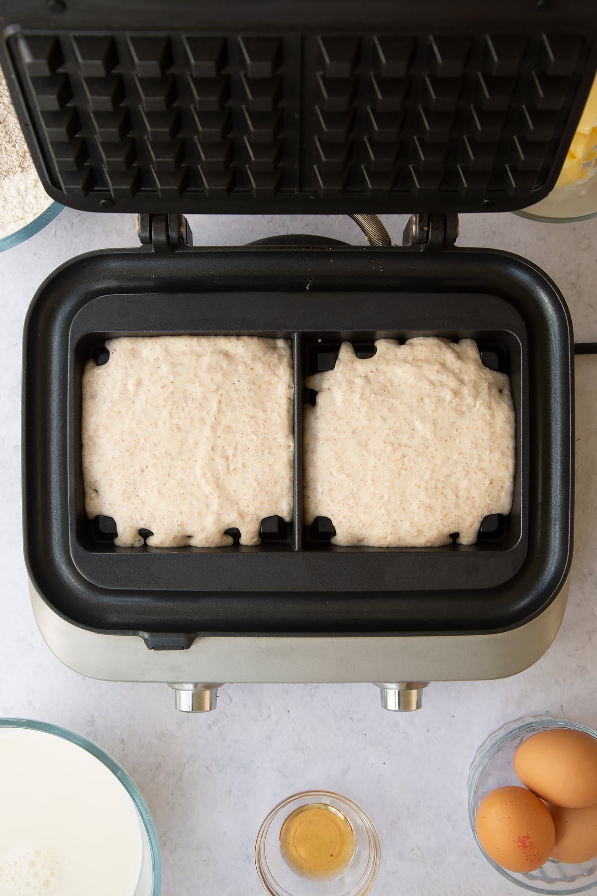 wholemeal waffle batter in 2 compartments of a waffle maker.