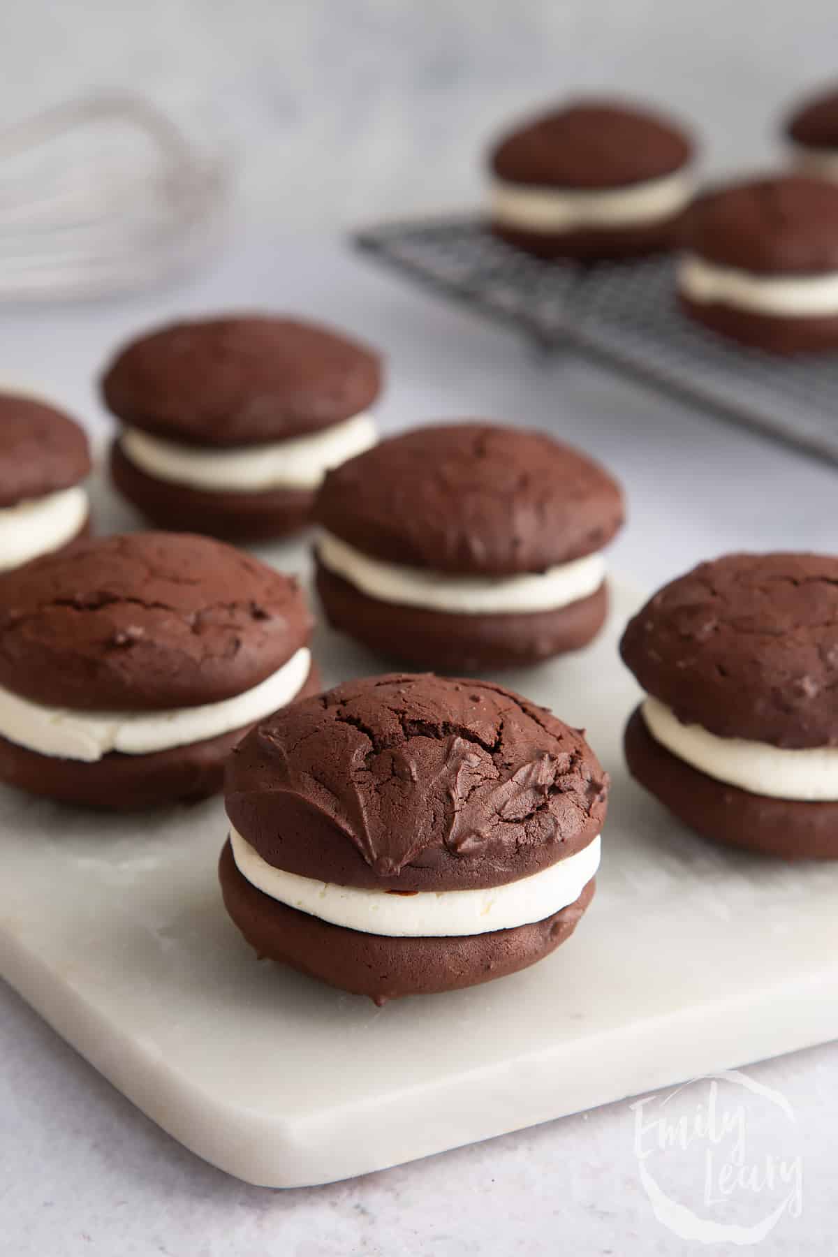 a marble chopping board filled with chocolate whoppie pies on a plain background.