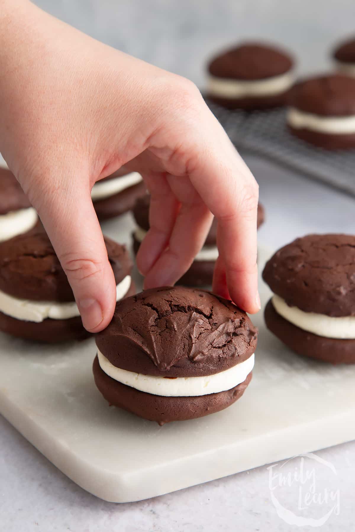 a hand picking up a Whoopie pie from a marble chopping board.