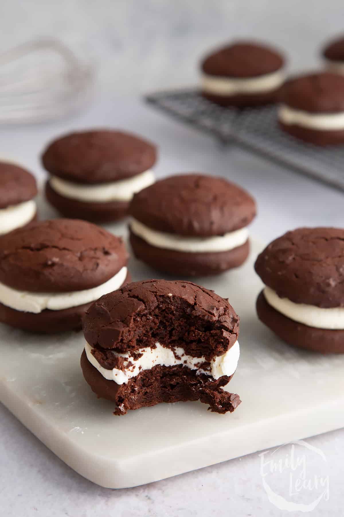 6 Whoopie pies on a marble chopping board with a bite missing from the nearest one.